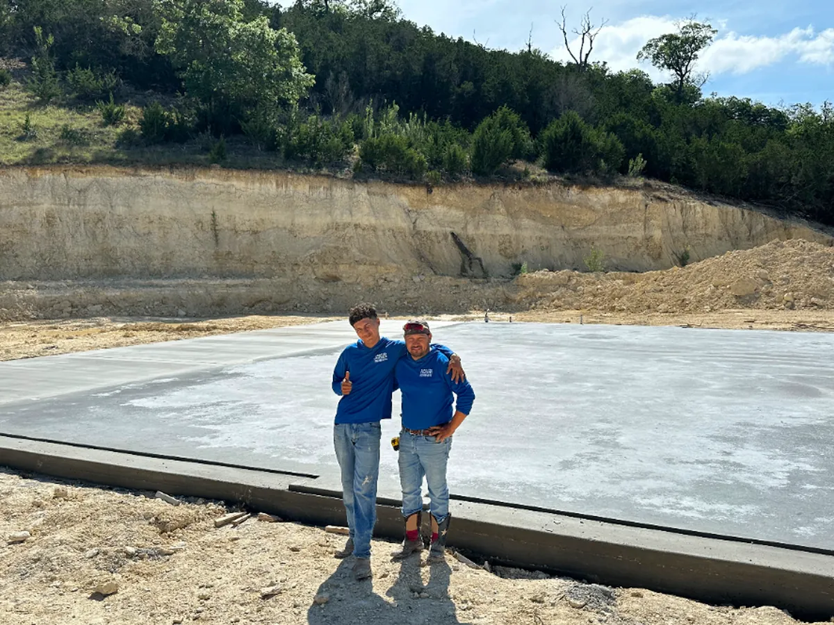 The Camacho Concrete owner and his son standing in front of a finished concrete foundation slab in the Texas Hill Country
